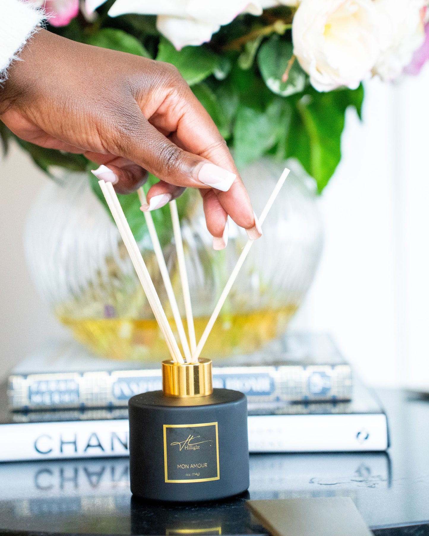 Hand holding a diffuser with flowers and books in the background