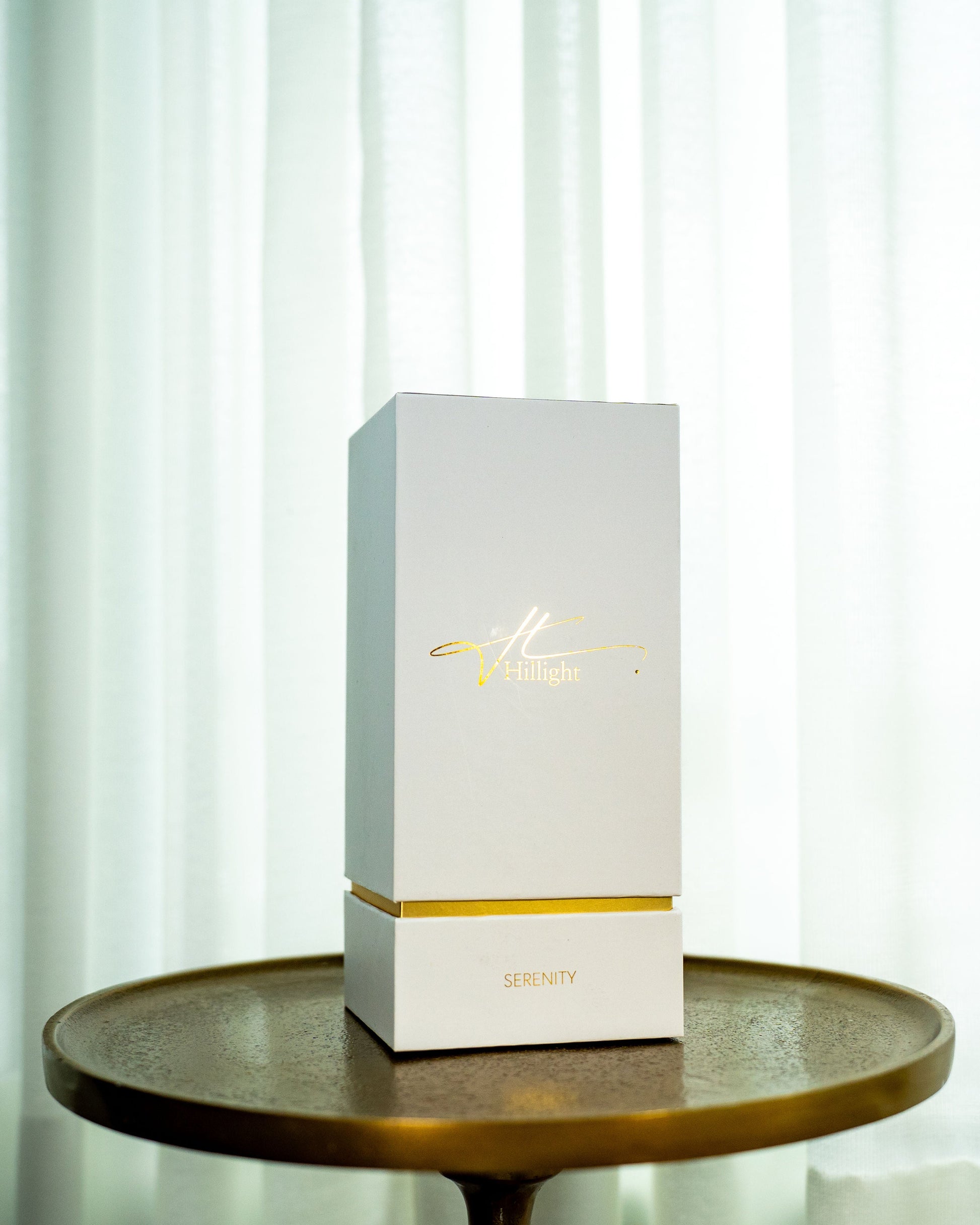 White box with gold accents on a wooden table against a white curtain background