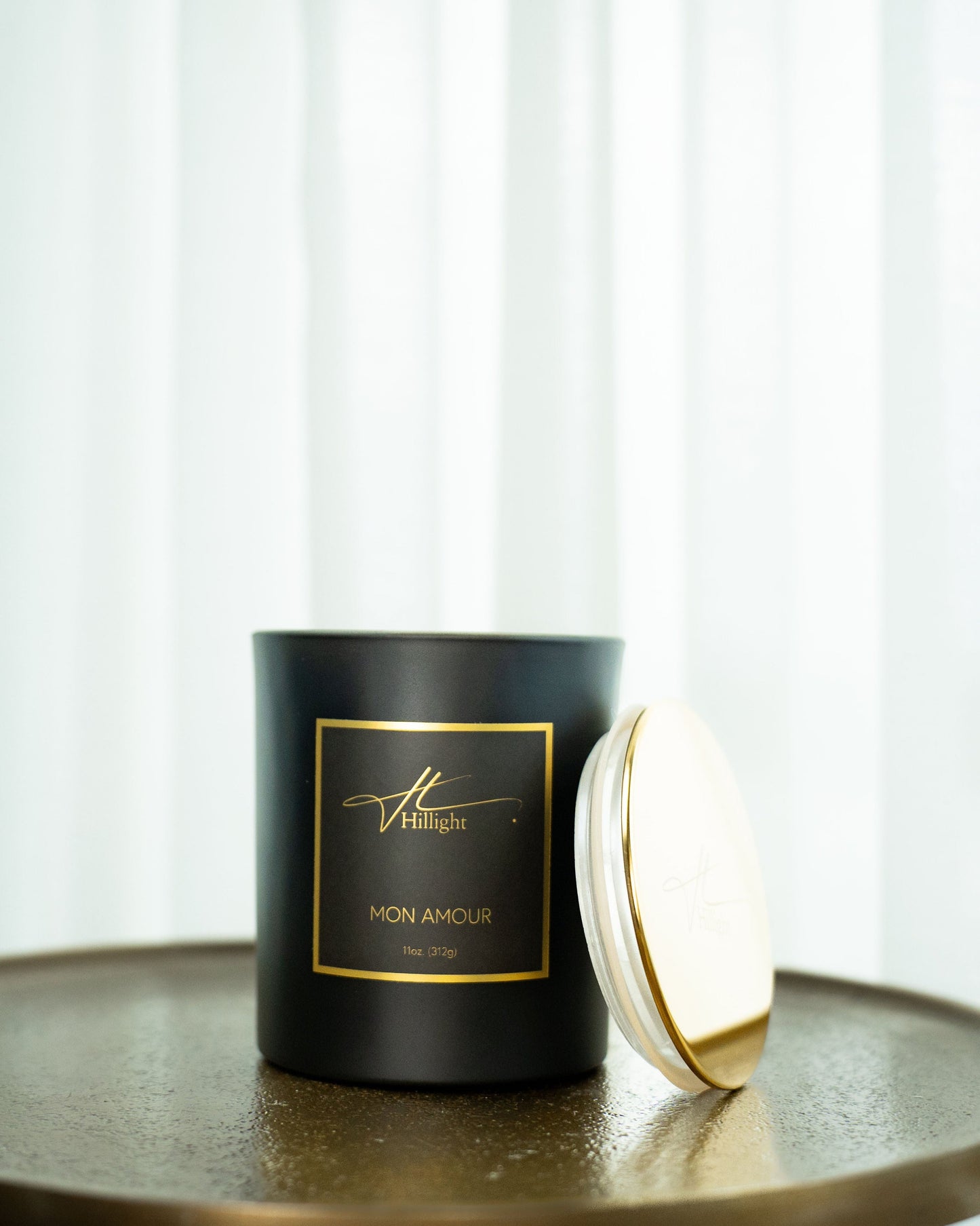 Black candle with gold lid on a reflective surface, white background