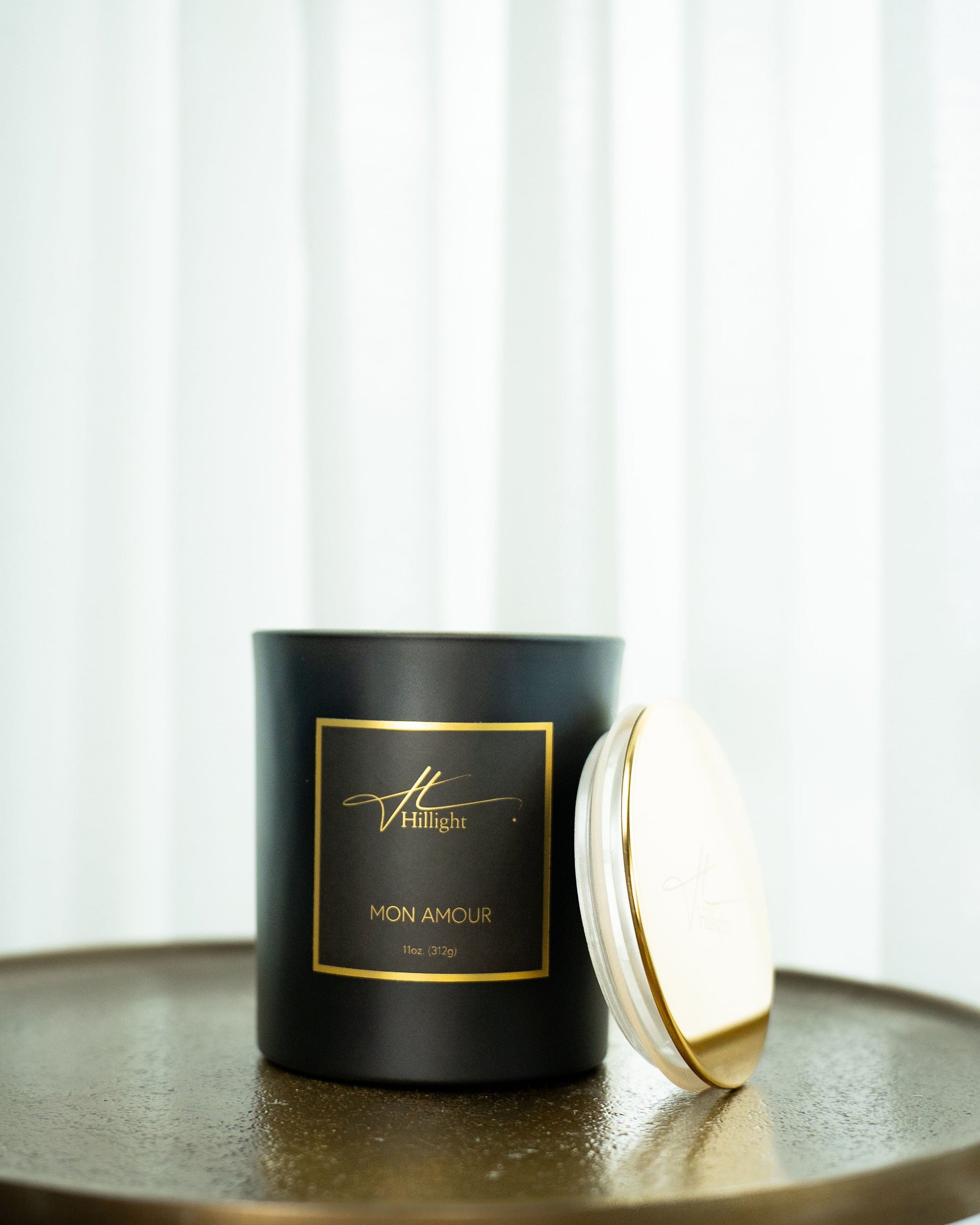 Black candle with gold lid on a reflective surface, white background